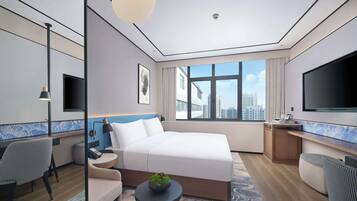 Habitación de hotel moderna con una cama grande, un escritorio, un televisor y vistas a la ciudad.