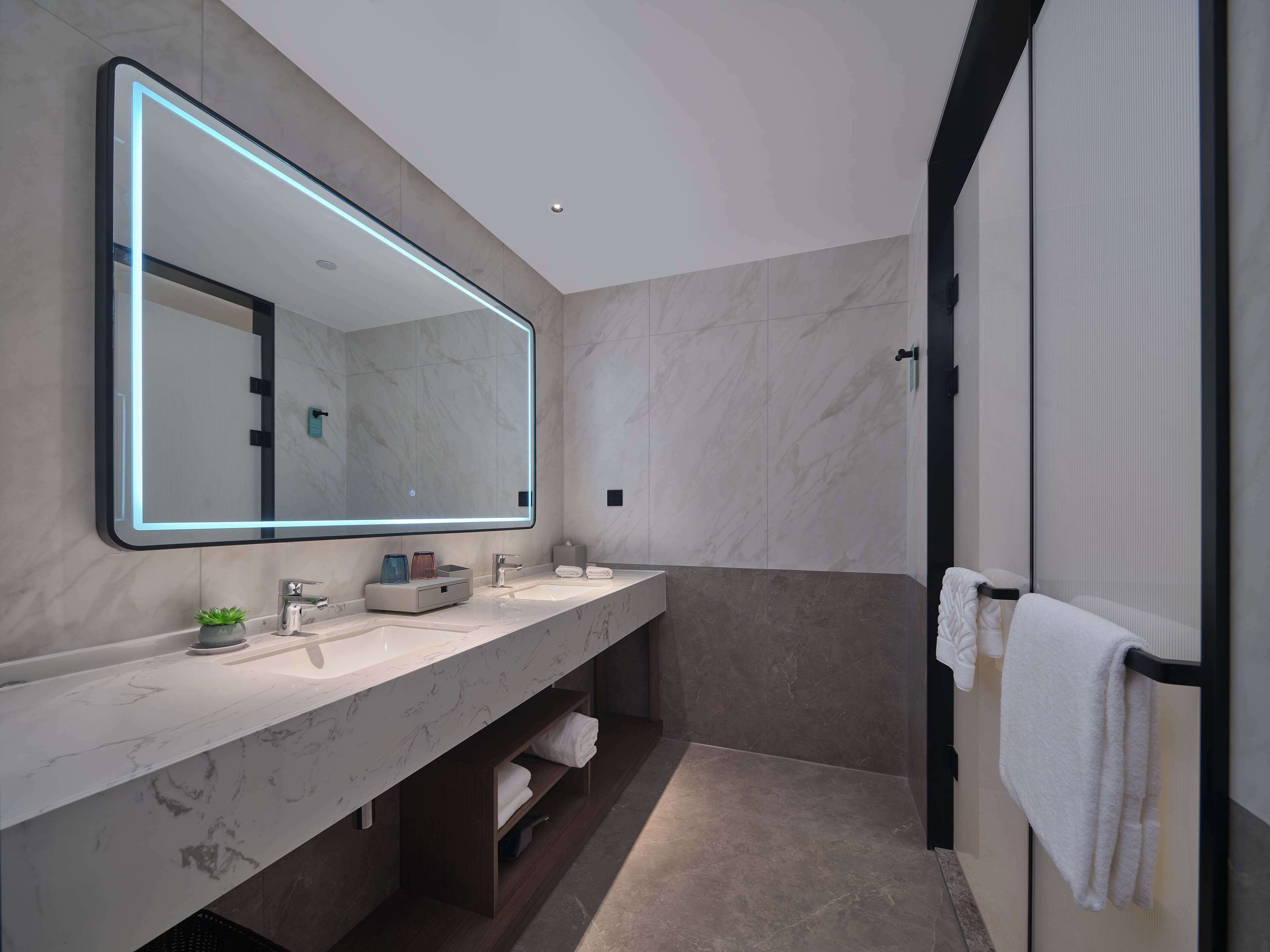 Un baño moderno con un espejo grande, dos lavamanos y un perchero para toallas.
