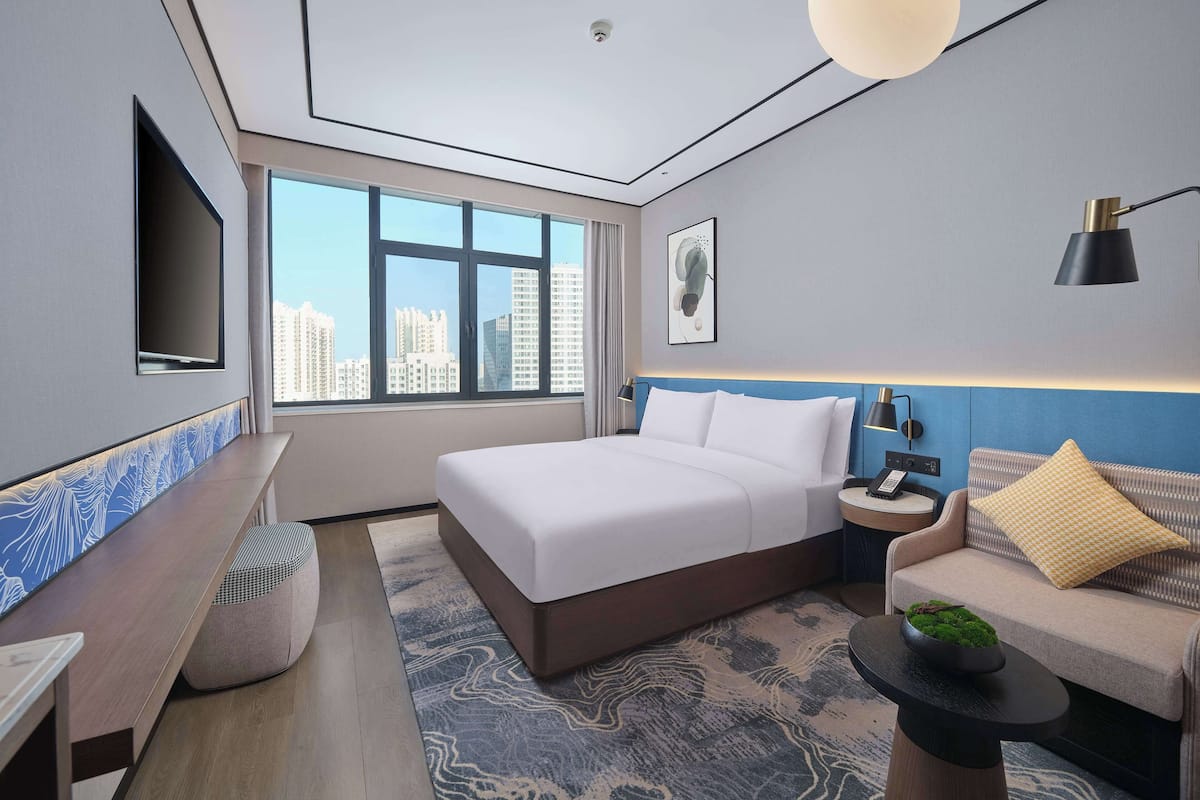 Quarto de hotel moderno com uma cama grande, área de estar, TV e vista para a cidade.