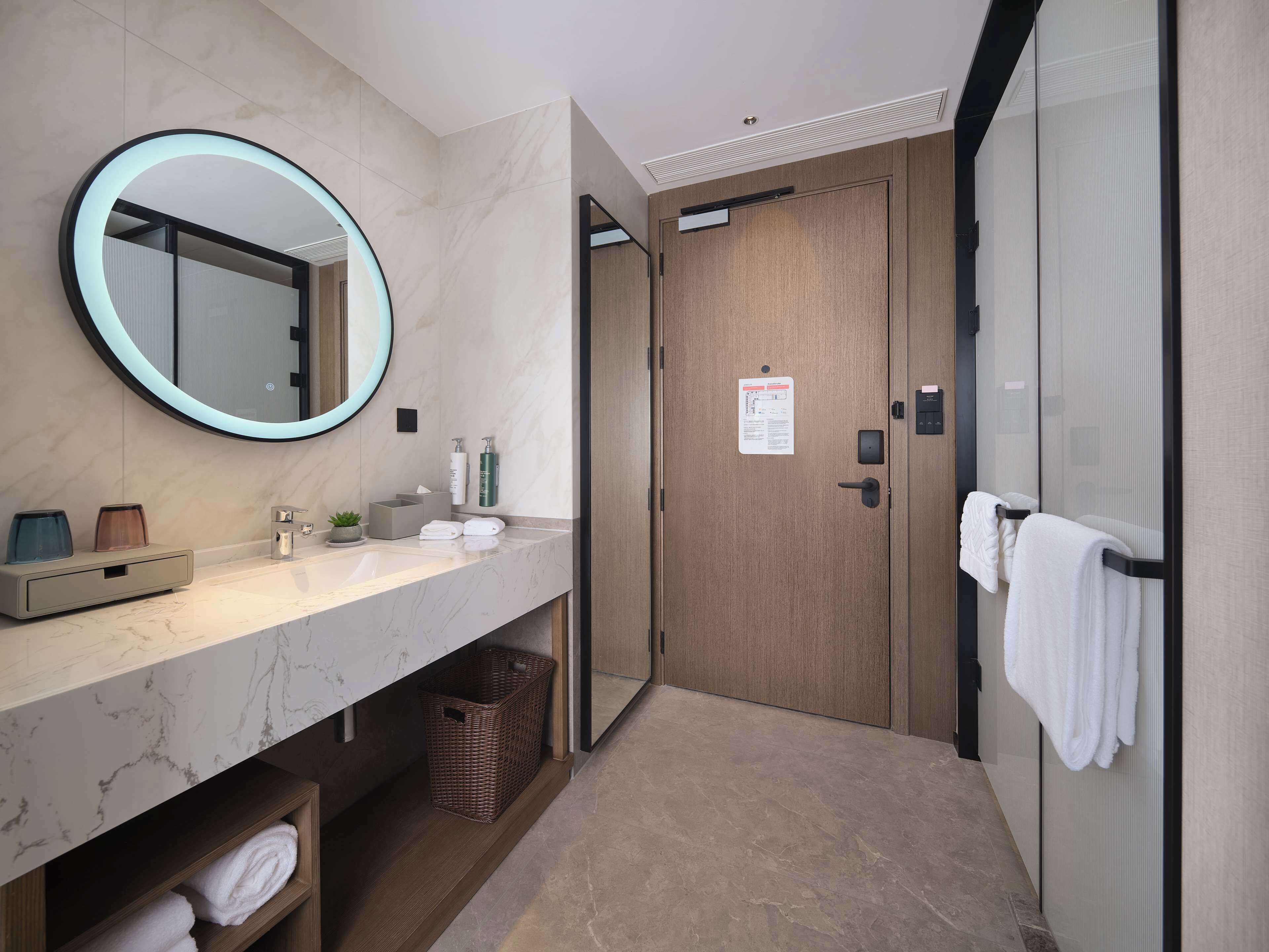 Un baño moderno con tocador de mármol, un espejo redondo, una puerta de madera y un perchero para toallas.