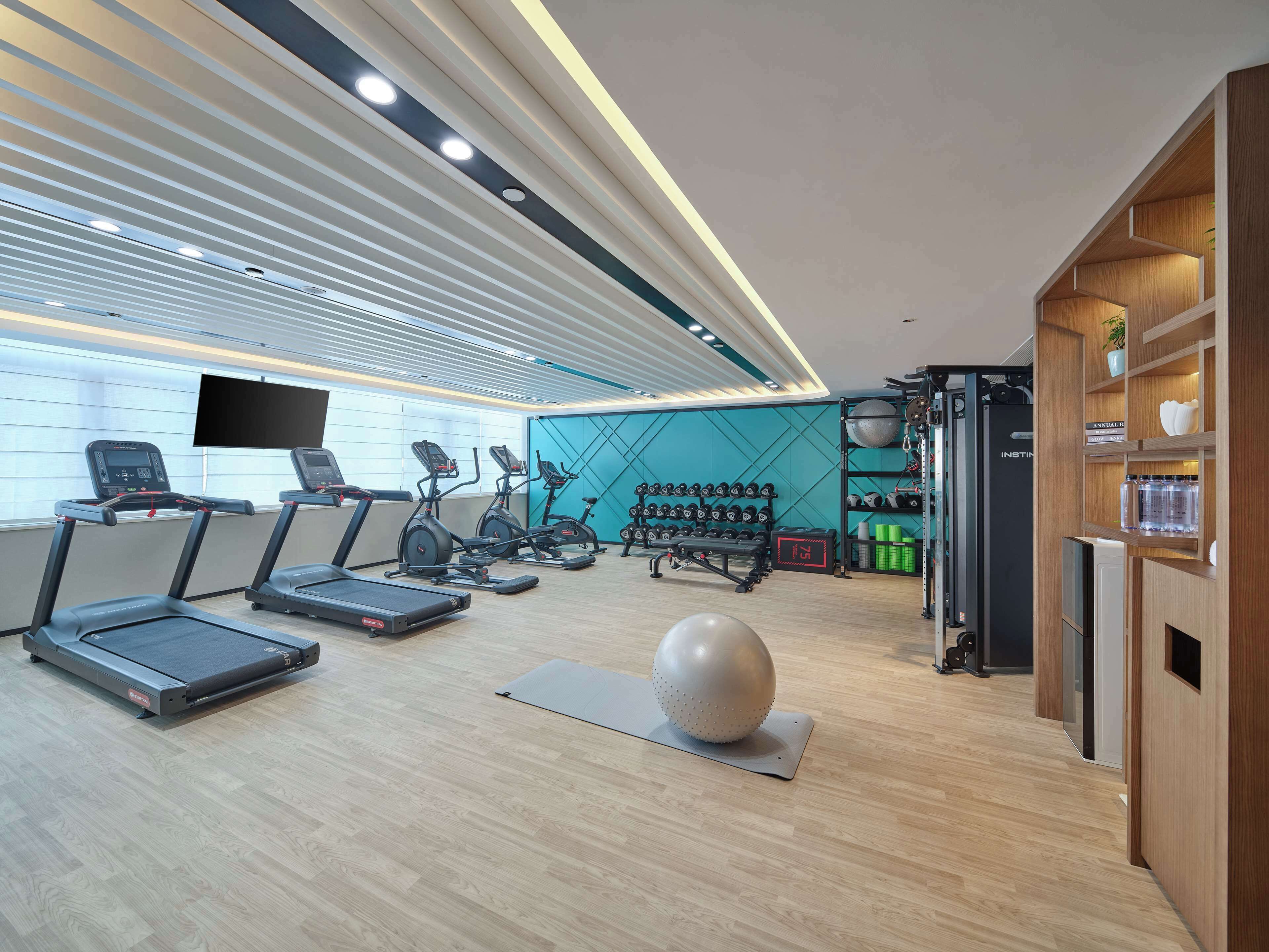 Un gimnasio moderno con cintas de correr, elípticas y una pelota grande de ejercicio.