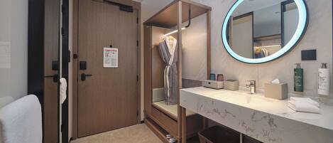 Une salle de bain moderne avec une porte en bois, un miroir doté d’un éclairage circulaire, un meuble-lavabo avec un plan de travail en marbre et un porte-serviettes.