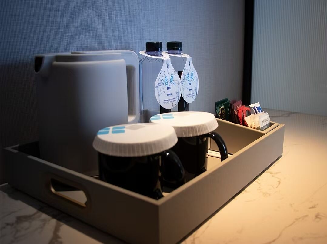 A tray with a kettle, two mugs, and two bottles of water, along with some snacks and a small box.