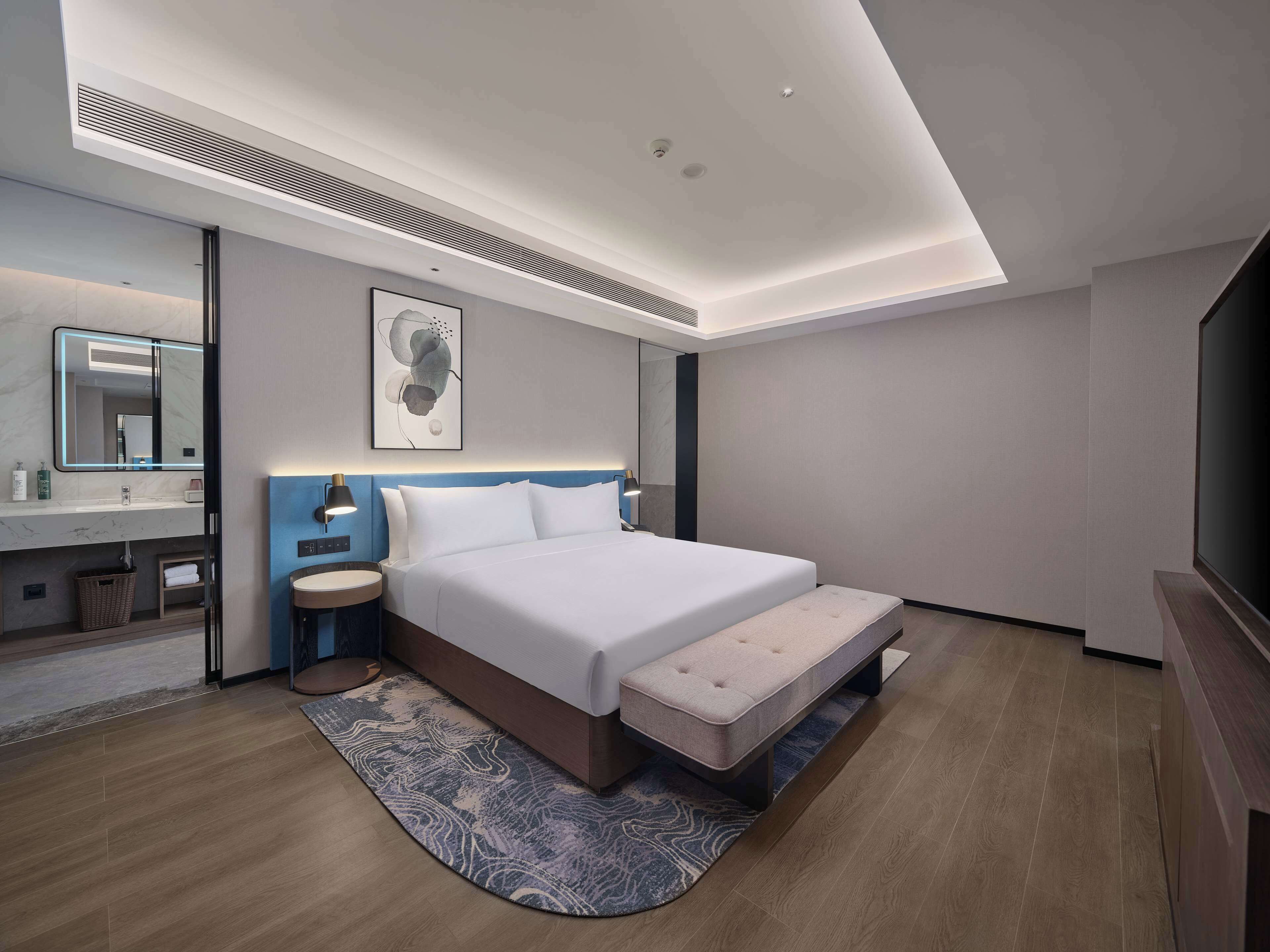 Une chambre d’hôtel moderne avec un grand lit, des tables de chevet, un miroir et un téléviseur à écran plat.