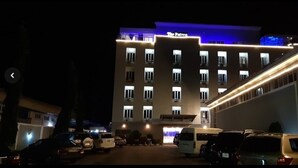 A hotel with multiple floors, a central entrance, and a parking area with several vehicles. - The Patron Hotel Suites Lekki (Lekki)