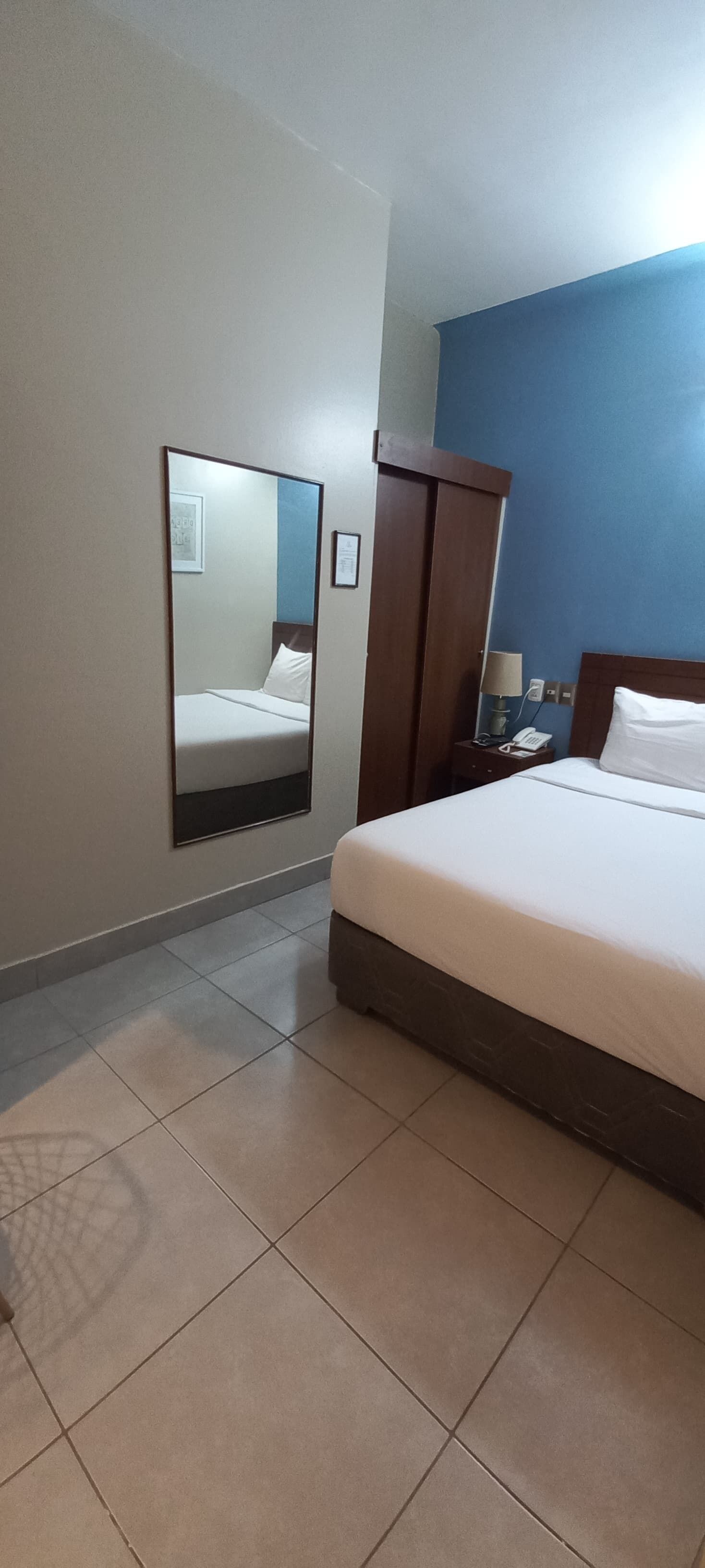 Ein Hotelzimmer mit Bett, Nachttisch, Spiegel und Kleiderschrank.