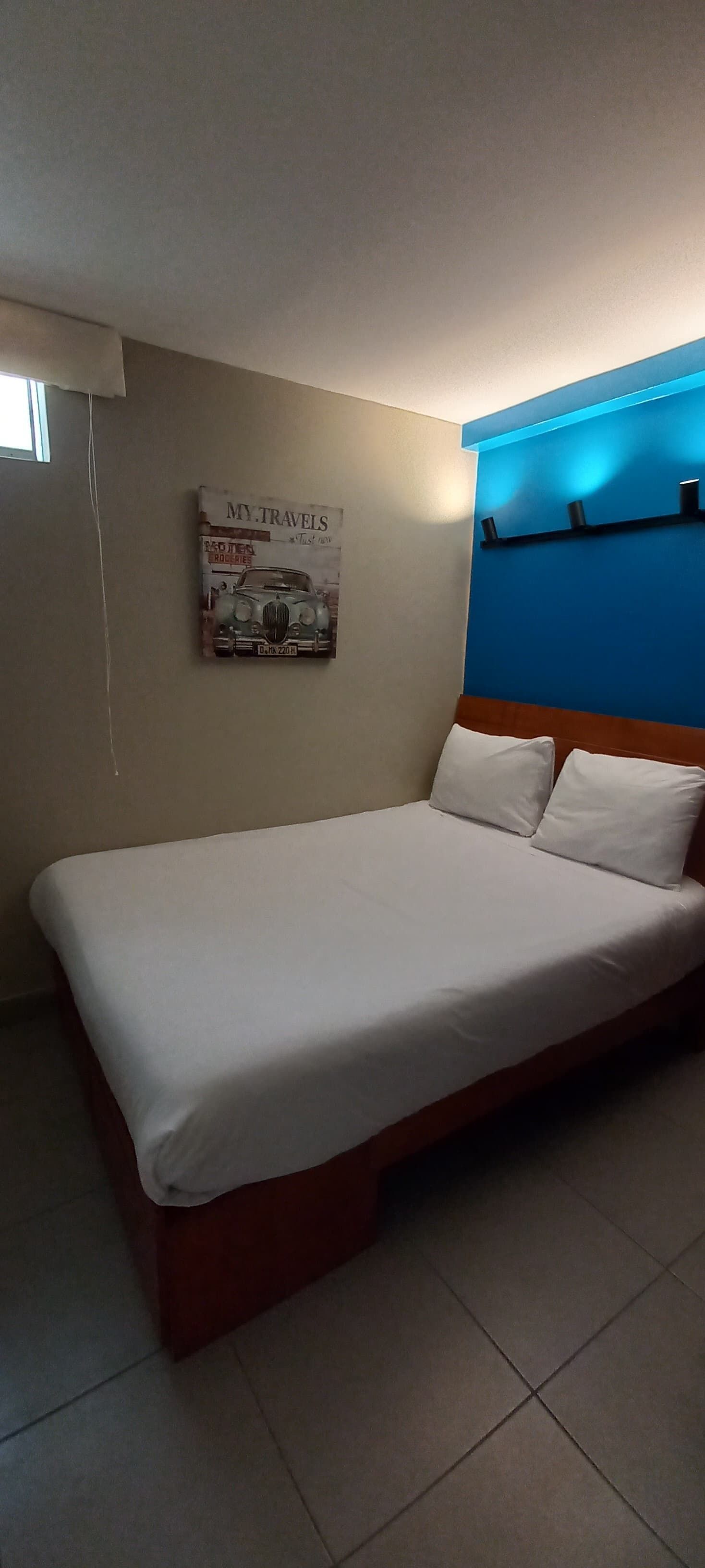 A single bed with white bedding in a room with a blue accent wall and a poster on the wall.