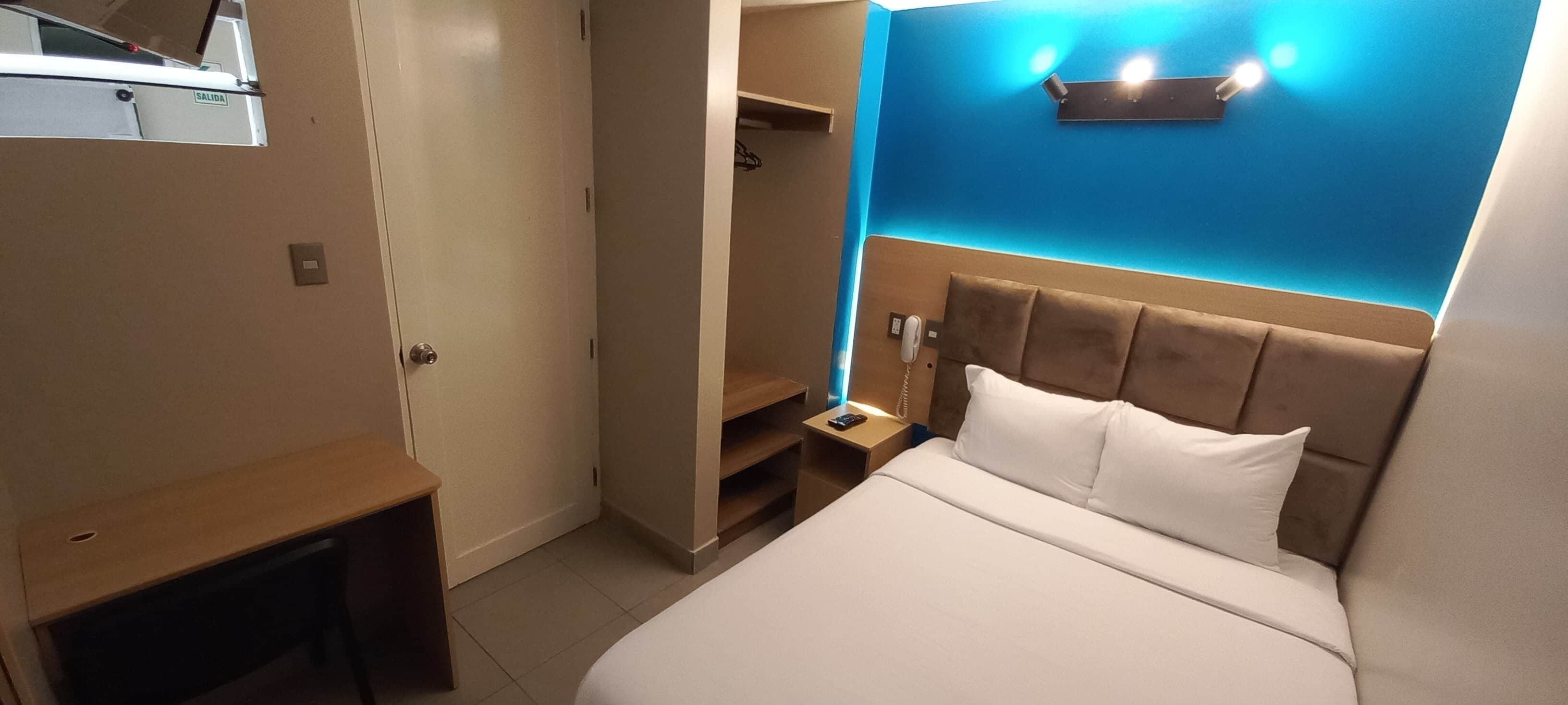 A hotel room with a bed, bedside table, and a wardrobe.
