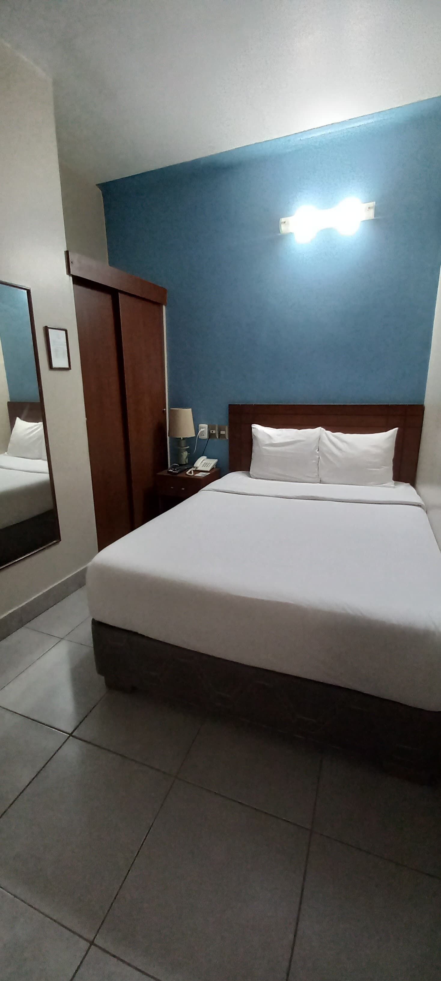 Une chambre d’hôtel avec un grand lit, une table de chevet, une lampe, un miroir et une armoire.