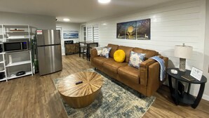 A modern living room with a brown leather sofa, a wooden coffee table, and a dining area with a table and chairs. - Couples Cabin at the Lake (Heber Springs)
