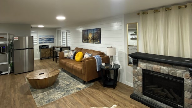 A modern living room with a fireplace, a sofa, a coffee table, and a dining area in the background. - Couples Cabin at the Lake (Heber Springs)