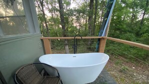A freestanding bathtub on a balcony with a wicker chair and a bucket. - Couples Cabin at the Lake (Heber Springs)