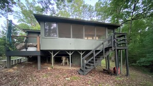 A cabin with a wooden deck, a staircase, and a covered area with a chair. - Couples Cabin at the Lake (Heber Springs)