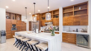 Een moderne keuken met een centraal eiland, een paar barkrukken, houten kastjes, roestvrijstalen apparatuur en hanglampen.