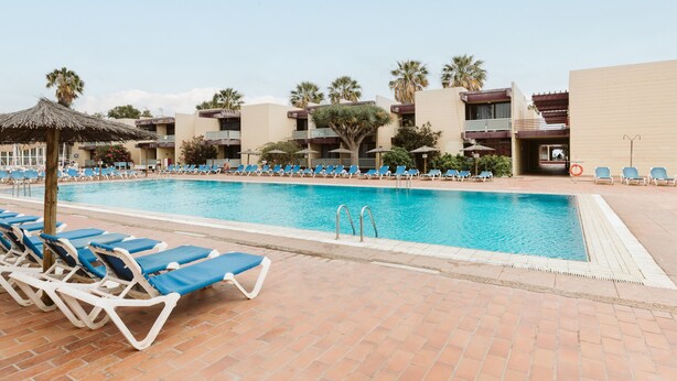 A poolside area with lounge chairs, a swimming pool, and a building with balconies. - Costa del Silencio: Private Terrace & Pool (Arona)