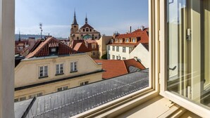 Vista desde una ventana que da a un paisaje urbano con arquitectura tradicional, incluyendo una iglesia con aguja y techos de tejas rojas.