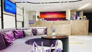 A modern lobby with a curved sofa, a reception desk, a large TV screen, and a mural of a sunset. - Lavande Hotel (Huizhou Huiyang Station) (Huizhou)