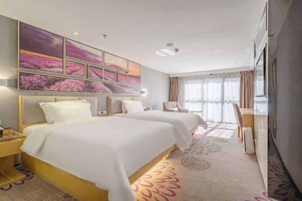 A hotel room with two beds, a desk, and a large window with curtains.