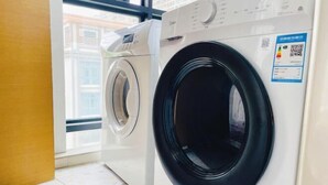 A laundry room with two washing machines, a QR code on the wall, and a window with a view of buildings. - Lavande Hotel (Huizhou Huiyang Station) (Huizhou)