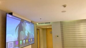 A hotel room with a large flat-screen TV mounted on the wall, a bed with white bedding, a bedside table, and a small trash bin. - Lavande Hotel (Huizhou Huiyang Station) (Huizhou)