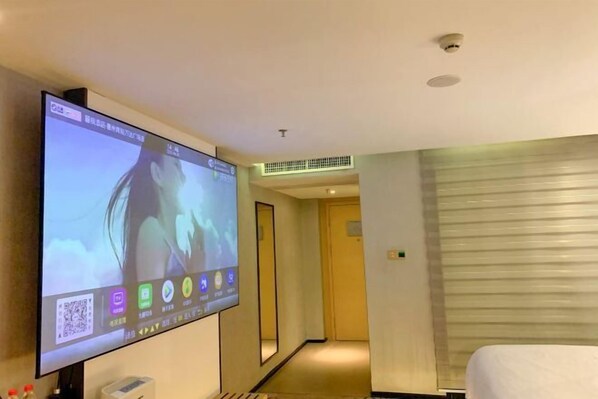A hotel room with a large flat-screen TV mounted on the wall, a bed with white bedding, a bedside table, and a small trash bin. - Lavande Hotel (Huizhou Huiyang Station) (Huizhou)