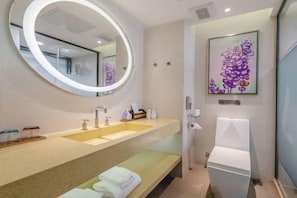 A modern bathroom with a round mirror, dual sinks, a toilet, and a framed floral artwork on the wall. - Lavande Hotel (Huizhou Huiyang Station) (Huizhou)