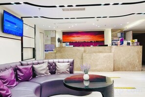 Un hall d’hôtel moderne avec un comptoir d’accueil, un grand téléviseur à écran plat, un canapé et une table basse.