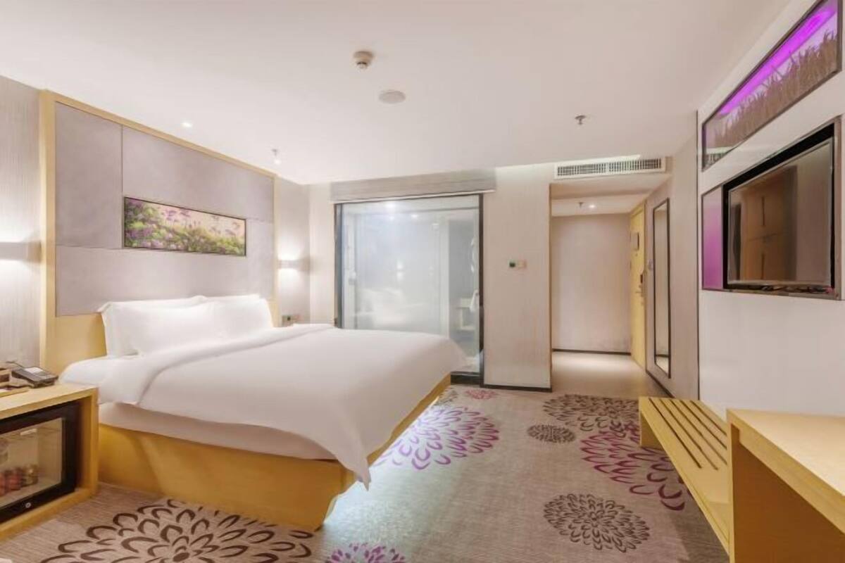 A hotel room with a bed, bedside table, TV, and a sliding door leading to a bathroom.