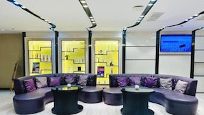 A modern lounge area with a curved sofa and round tables, a television screen, and illuminated shelves with products. - Lavande Hotel (Huizhou Huiyang Station) (Huizhou)