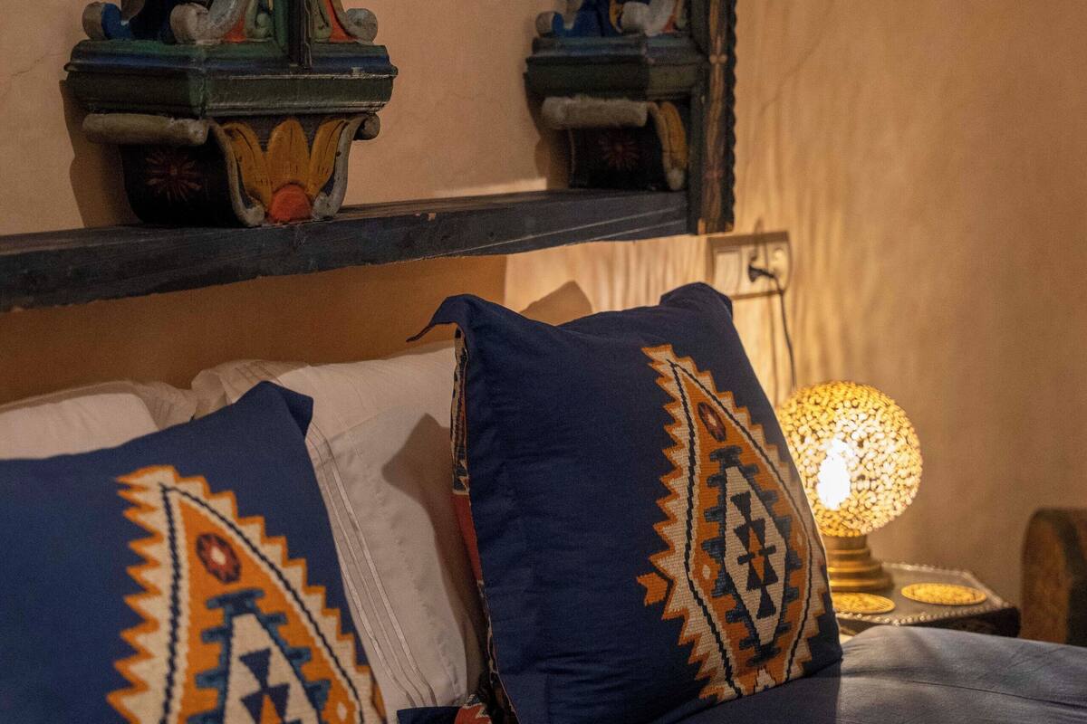 A bed with blue bedding and patterned pillows, a decorative wall with intricate designs, and a lamp on a bedside table.