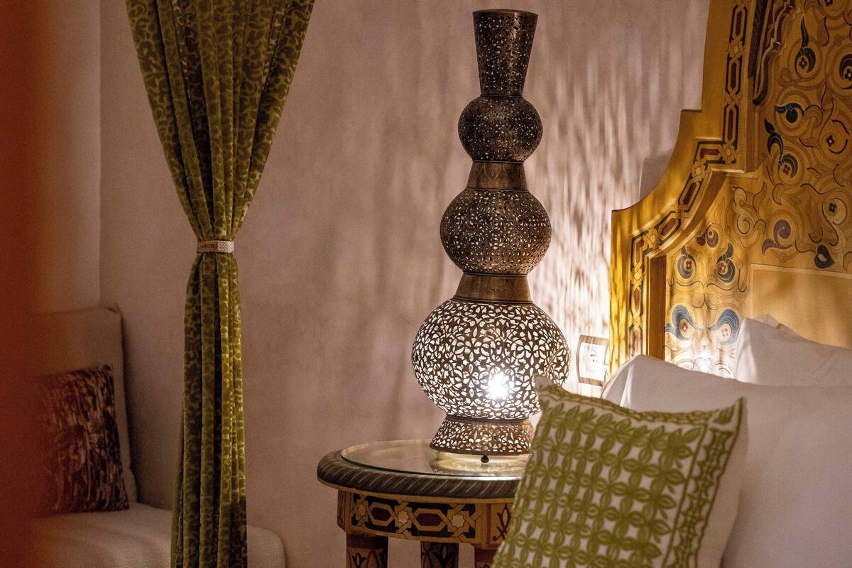A bed with a green patterned bedspread, a decorative lamp, and a green pillow on a nightstand.