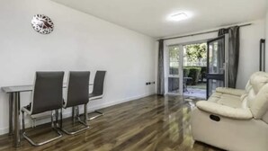 A modern living room with a sofa, a dining table with chairs, and a large window. - Cosy Feltham Apartment With 2 Bedrooms (Feltham)