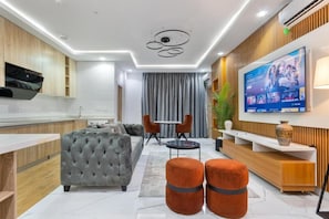 A modern living room with a grey sofa, orange ottomans, a TV, and a wooden cabinet.