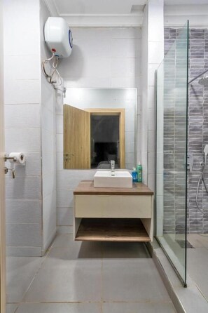 A bathroom with a white tiled wall, a wooden vanity with a sink, a mirror, and a glass shower enclosure.