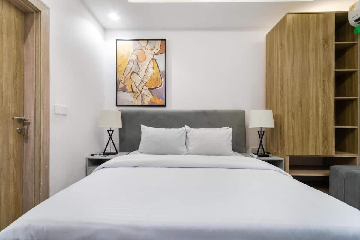 Un cuarto de hotel ordenado con una cama grande, dos mesitas de noche con lámparas, un armario de madera y un cuadro abstracto enmarcado en la pared.