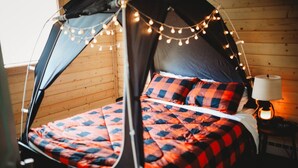 Ein gemütliches Zeltenbett mit karierter Decke, Baldachin und Lichterketten.