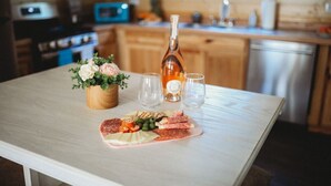 Ein Holztisch mit einer Wurstplatte, einer Weinflasche und Gläsern in einer Küche.