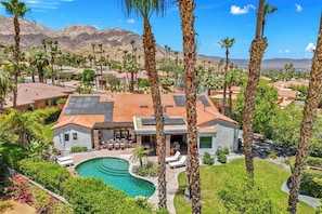 Una casa grande con piscina, rodeada de palmeras y montañas.
