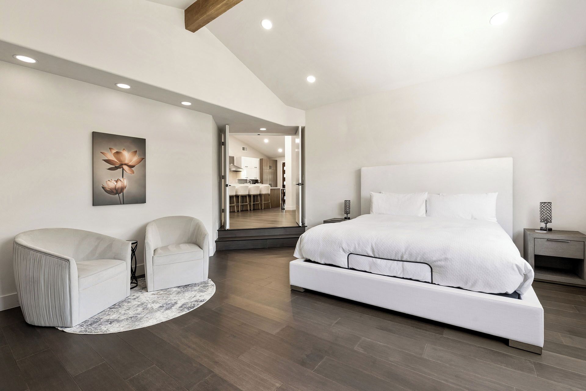 Une chambre à coucher moderne avec un grand lit, deux fauteuils, une petite table et un tableau au mur.
