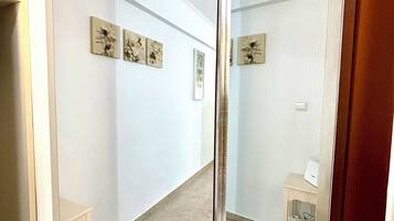Un pasillo con un espejo que refleja una habitación, una mesita pequeña y obras de arte en las paredes.