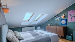 A bedroom with a sloped ceiling, skylights, a bed, a wooden dresser, and wall art. - Kraków Castle View - Spacious Apartment - by Rentujemy (Kraków)