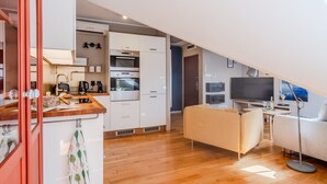 A compact kitchen with modern appliances, a dining area with a sofa, and a TV in a loft-style living space. - Kraków Castle View - Spacious Apartment - by Rentujemy (Kraków)