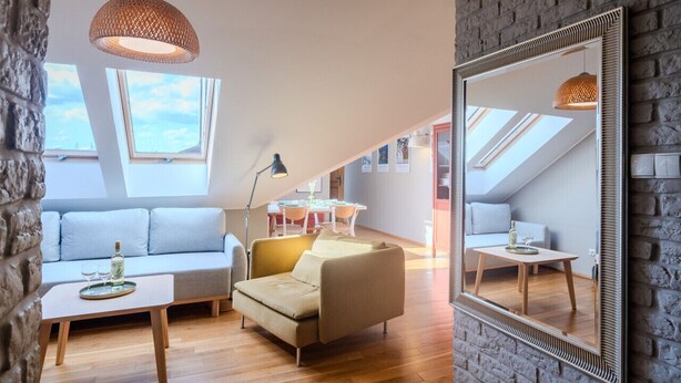 A modern loft apartment with a stone wall, a large mirror, a sofa, a coffee table, and a dining area with a table and chairs. - Kraków Castle View - Spacious Apartment - by Rentujemy (Kraków)