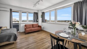 Une chambre moderne équipée d’un lit, d’un canapé, d’une table à manger pour deux personnes et de grandes fenêtres offrant une vue sur la ville.