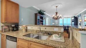 A kitchen with granite countertops, stainless steel sink, wooden cabinets, and a view of the ocean. - Closest 2 Bedroom to Beach Spectacular Gulf, Pier, & 🐬 View at A403 Waterscape (Fort Walton Beach)