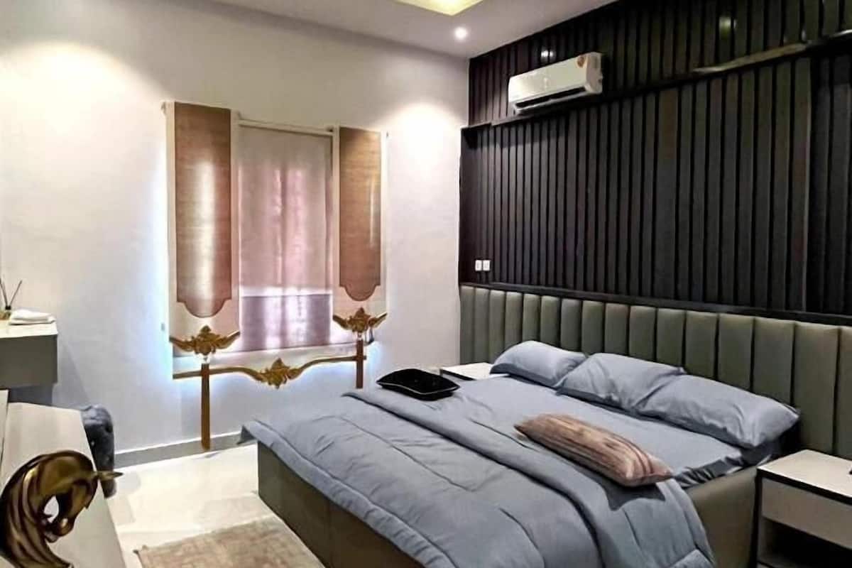 A modern bedroom with a bed, bedside tables, a nightstand, a window with curtains, and a wall-mounted air conditioner.