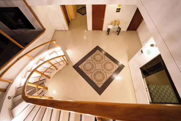 A spacious lobby with a central decorative rug, a staircase with wooden railings, and a reception desk. - Hostal Los Balcones (Nazca)