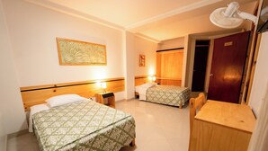 Ett hotellrum med två sängar, ett skrivbord i trä, en stol, en fläkt och en dörr med nummerlappen "401".