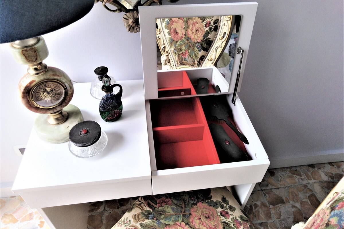 Ein weißer Nachttisch mit Spiegel, einer Messing-Uhr und einem kleinen Glasbehälter.