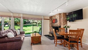 A living room with a fireplace, a TV mounted on the wall, a dining table with chairs, and a leather sofa. - Lichenhearth 08 (Snowmass Village)